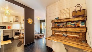Een moderne keuken met een houten kookeiland, een eethoek met een witte stoel en een gezellige zithoek met een bed en uitzicht op de natuur.