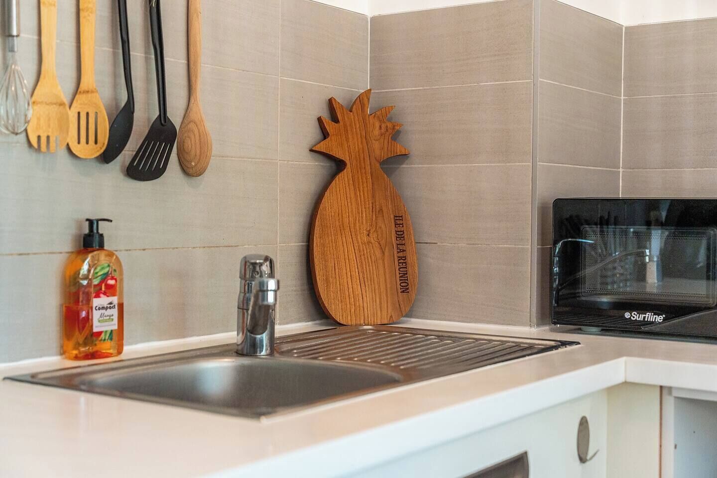 A kitchen with a stainless steel sink, a Surfline microwave, wooden utensils, and a soap dispenser.