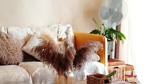 Een rustieke houten tafel met een vaas gedroogd pampa gras, een geweven mand en een ventilator op de achtergrond.