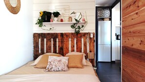 Een slaapkamer met een houten hoofdbord, een bed met beige beddengoed, en een wandplank met planten en decoratieve objecten.