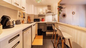 Een compacte keuken met witte kasten, een koffieapparaat, een magnetron en een broodrooster. Er is een kleine oven en een spoelbak met een houten aanrecht.