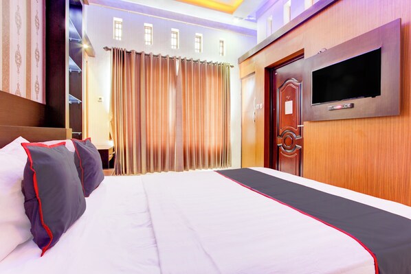Une chambre d’hôtel avec un grand lit, un téléviseur fixé au mur et une porte en bois.