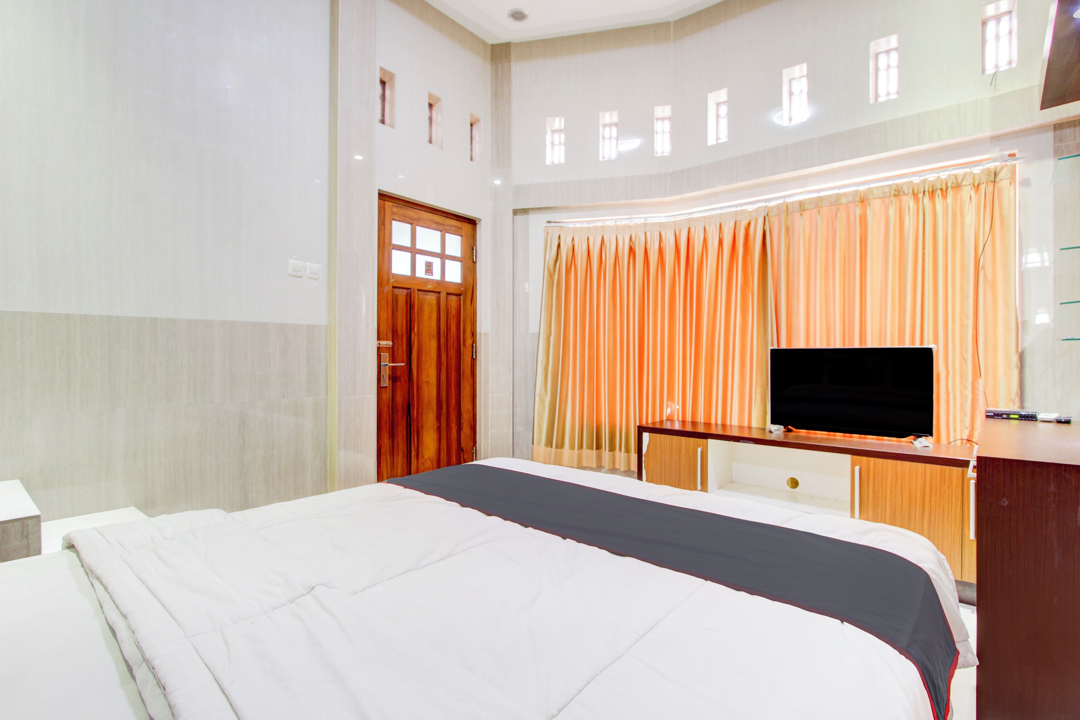 Una habitación de hotel con cama, escritorio con televisor y ventana con cortinas.