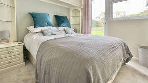 Une chambre à coucher comprenant un lit, des tables de chevet, une commode et une fenêtre donnant sur l’extérieur.