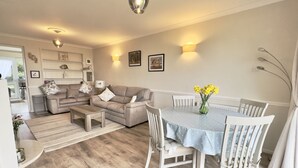 Un salon moderne avec un coin repas, comprenant un ensemble de canapés, une table basse, une table à manger avec des chaises et un vase de fleurs.