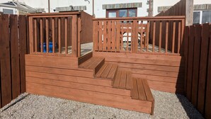 Une terrasse en bois avec une rampe menant à un espace surélevé, le tout entouré d’une clôture en bois.