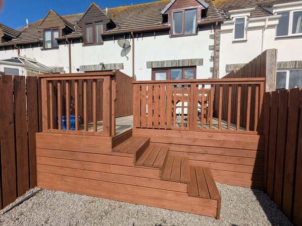 A wooden deck with a ramp leading to a raised platform, surrounded by a wooden fence.