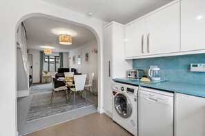 A modern kitchen with white cabinets, a washing machine, and a coffee maker.