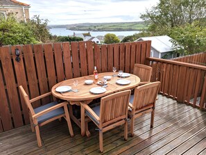 A wooden deck with a round table set for dining, surrounded by chairs.