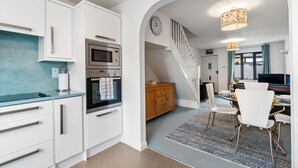 Une cuisine moderne avec des meubles blancs, un four à micro-ondes et un four traditionnel. On y trouve également un coin repas avec une table, des chaises et un escalier menant à un autre niveau.