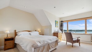 Une chambre à coucher avec un grand lit, une chaise, un bureau et une fenêtre donnant sur un beau paysage.