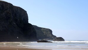 Una playa costera con un acantilado rocoso y una gran roca en el agua.