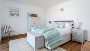 Un dormitorio con cama, mesitas de noche, una silla, cómoda y alfombra.