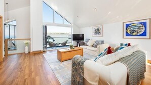 Un salón amplio con un ventanal grande, un conjunto de sofás, una mesa de centro y un televisor.