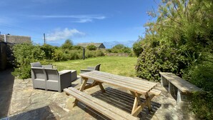 Eine Terrasse mit Holzbänken und Stühlen, einem Picknicktisch und einem Steinboden.