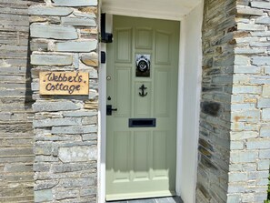 A stone wall with a green door and a sign reading 'Webb's Cottage.'