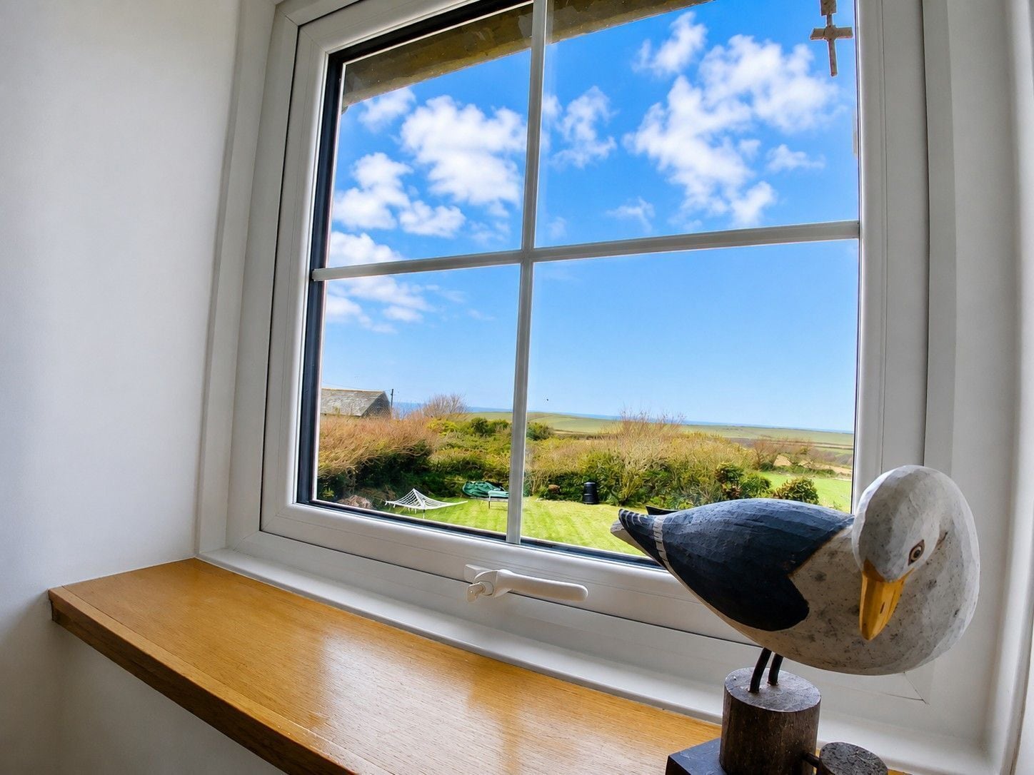 A room with a window overlooking a landscape, a wooden bench, and a bird sculpture.