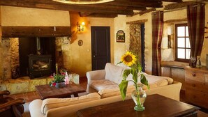 A rustic room with a stone fireplace, a sofa, a wooden coffee table, and a vase with a sunflower. - Farmhouse paradise with meadows, forests, animals (Issigeac)