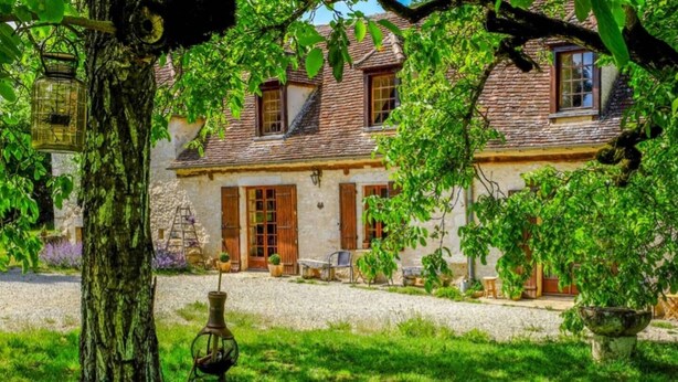 A rustic stone house with a gravel driveway, a wooden door, and a small porch area with outdoor seating. - Farmhouse paradise with meadows, forests, animals (Issigeac)