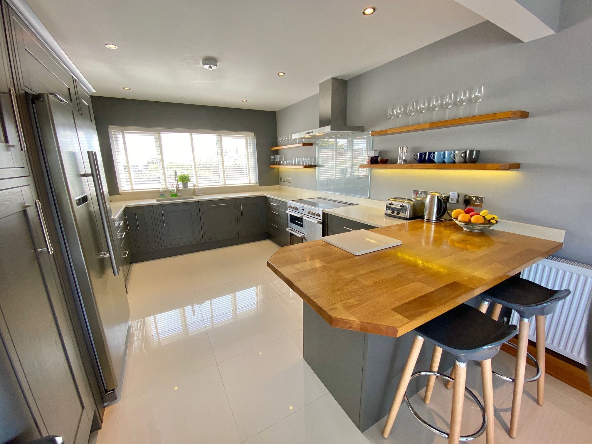 A modern kitchen with a central island, bar stools, and a bowl of fruit.