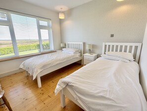 A bedroom with two single beds, wooden flooring, and a window with blinds.