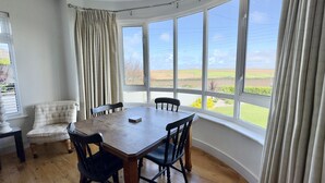 Ein Essbereich mit einem großen Tisch und Stühlen, einem gepolsterten Sessel und Blick auf die Landschaft durch große Fenster.