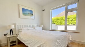 Ein Schlafzimmer mit einem großen Bett, zwei Nachttischen, einem Fenster mit Blick auf Grünflächen und einem gerahmten Bild an der Wand.