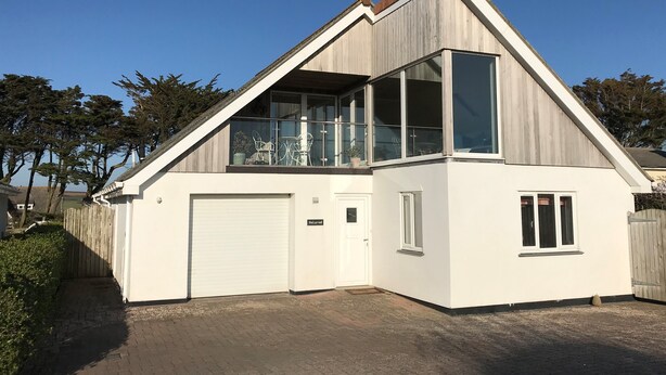 Une maison moderne à deux étages, dotée d’un garage, d’un balcon et de grandes fenêtres.