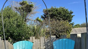 Dos sillas Adirondack turquesa en un jardín con una cerca de madera y árboles al fondo.