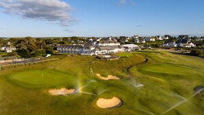 Un campo de golf con búnkeres, un club de campo y edificios residenciales al fondo.