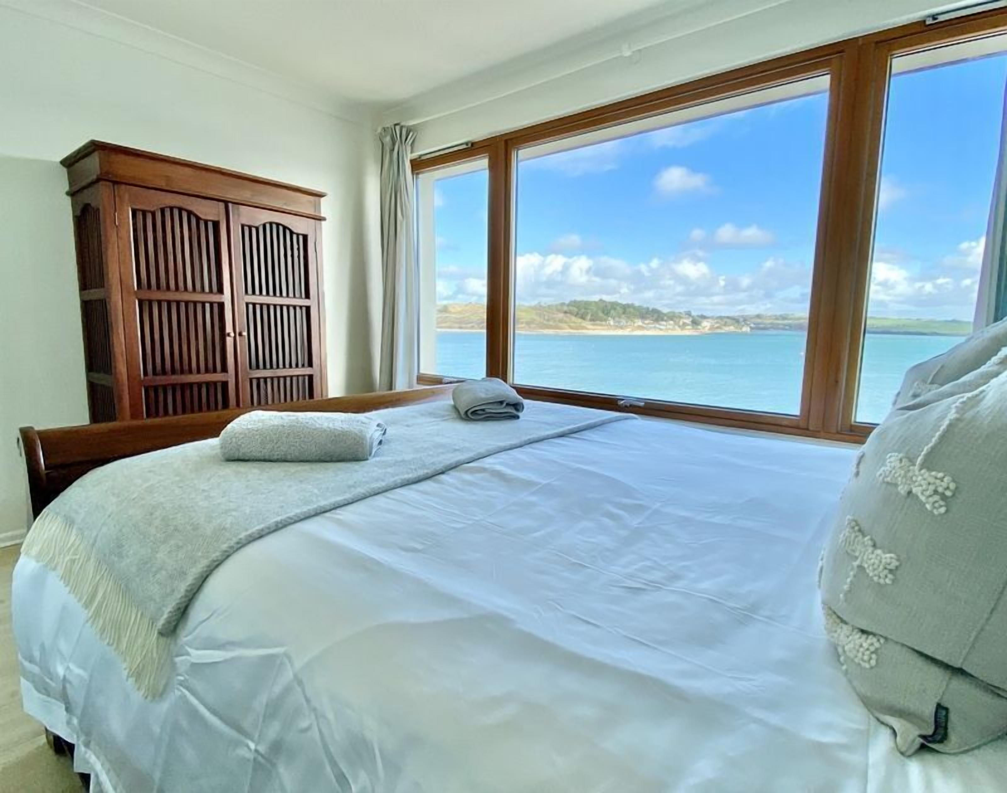 A bedroom with a large bed, a wooden wardrobe, and a view of the sea.