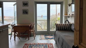 Ein Zimmer mit einem Bett, einem Schreibtisch und einem Stuhl. Zwei Fenster bieten Blick auf eine Brücke und Gebäude.