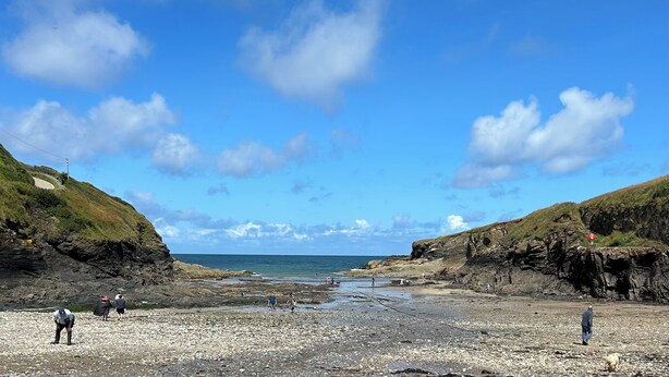 Ein felsiger Strand mit Spaziergängern und blauem Himmel.
