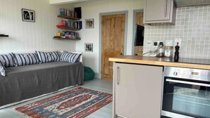 Eine kompakte Küche mit Backofen, kleiner Arbeitsplatte und grauem Sofa mit gestreiften Kissen.