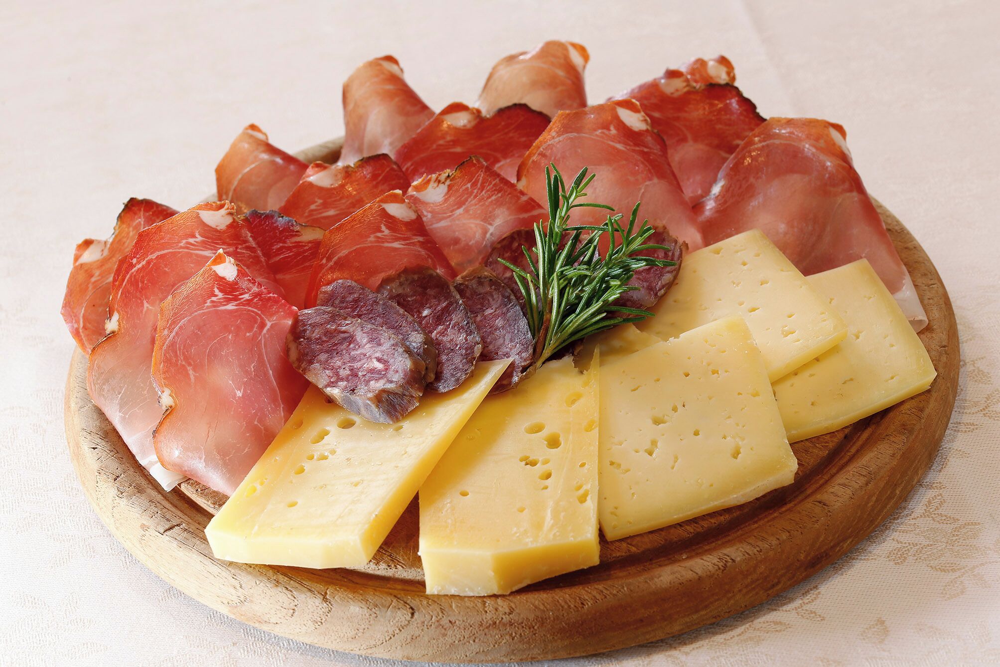 Ein Holzbruch mit einer Anordnung von geschnittenem Rohfleisch und Käse auf einer Tischdecke.