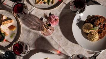 Una mesa dispuesta con diversos platos, copas de vino tinto y cubiertos, lo que sugiere una disposición para comer.
