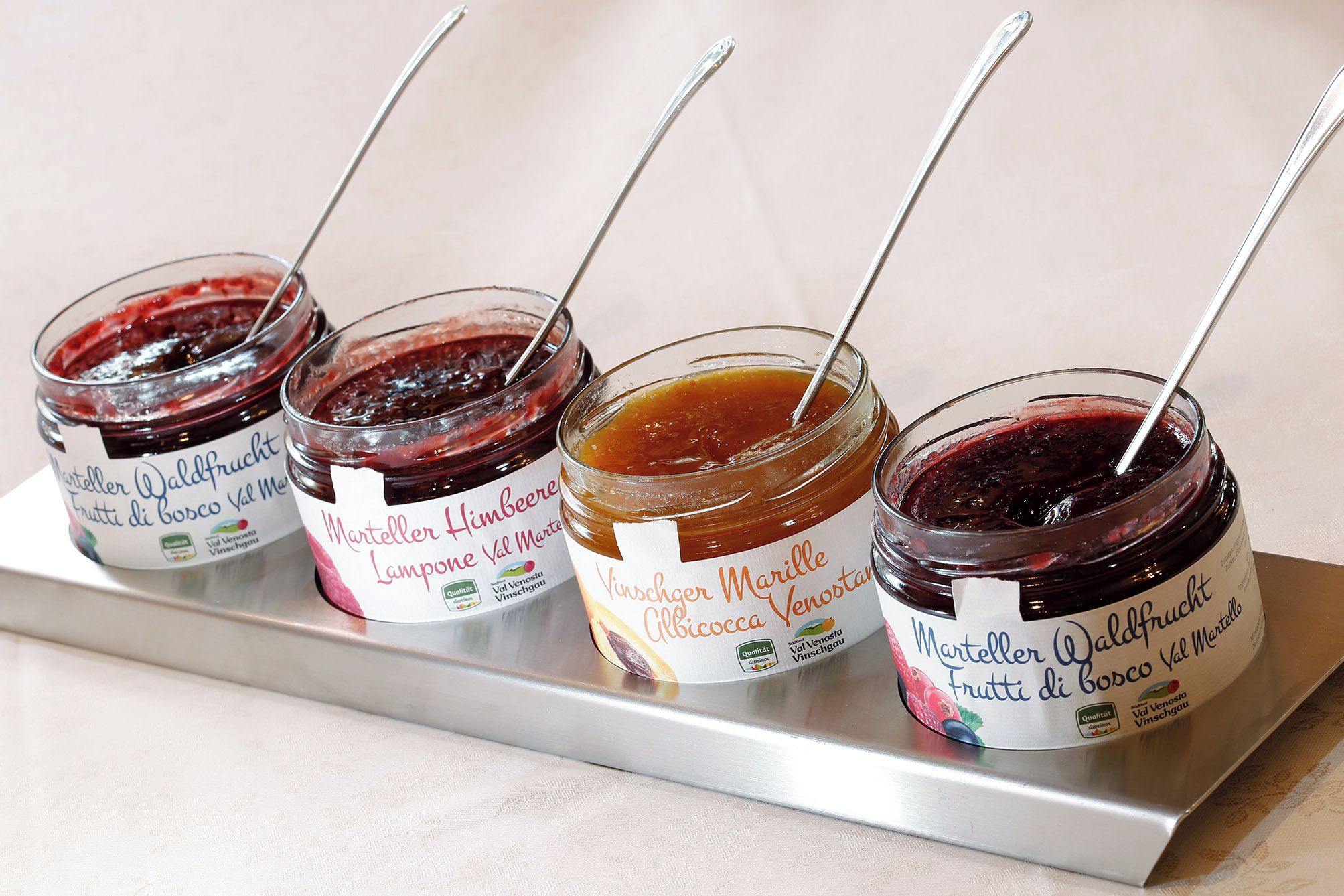 Four jars of fruit preserves on a metal tray.