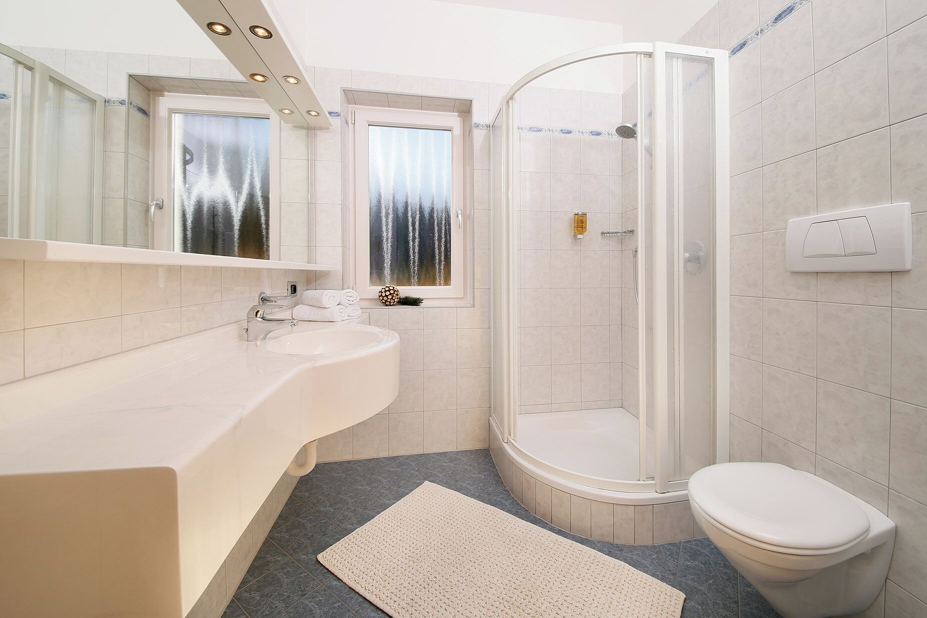 Ein modernes Badezimmer mit einer Glaskabine zur Dusche, einem weißen Waschbecken und einer Toilette.