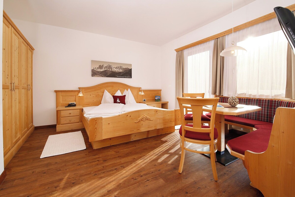 Une chambre à coucher avec un lit en bois, des tables de chevet, un bureau avec une chaise, une fenêtre avec des rideaux et une armoire en bois.