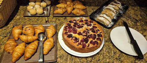 A variety of baked goods including croissants, a cherry pie, and pastries on a kitchen counter.
