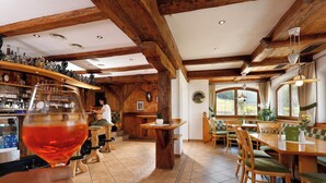 Un intérieur rustique avec des poutres en bois, un coin bar et un espace repas doté de chaises rembourrées de couleur verte.