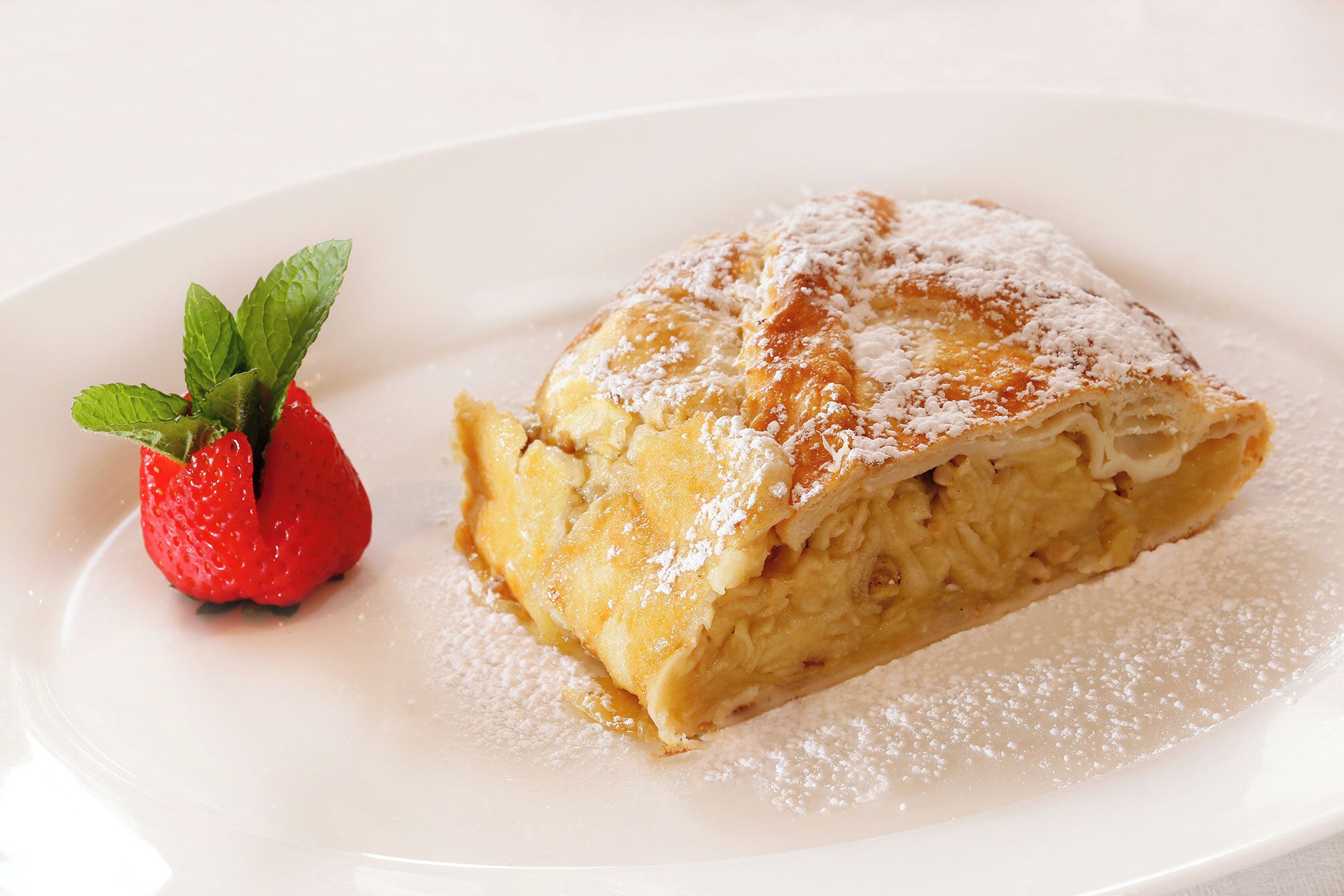 A slice of cake with powdered sugar and a strawberry on a white plate.