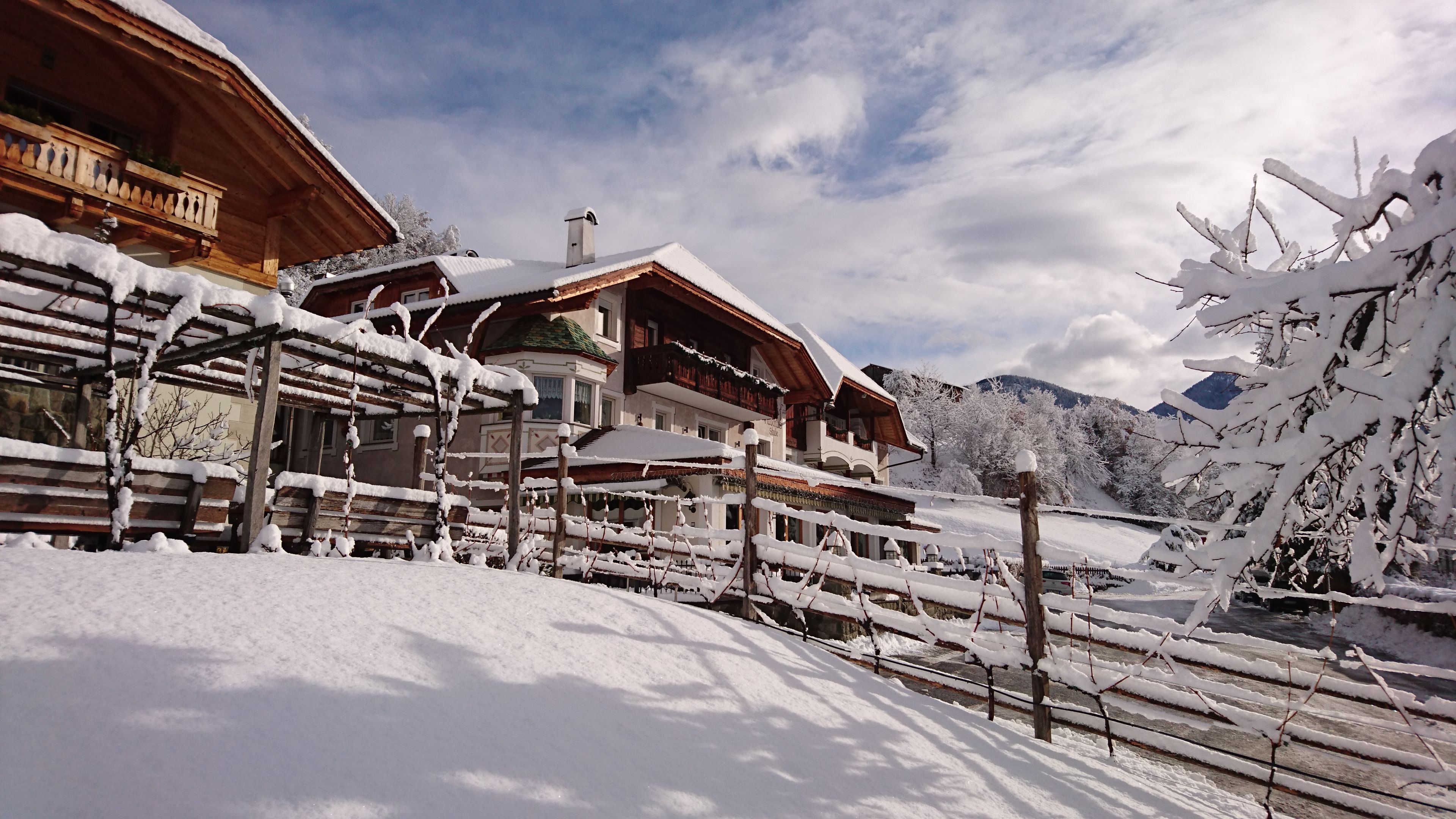 A wooden chalet with a balcony, surrounded by snow-covered trees and mountains.