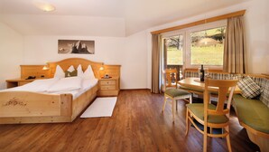 Une chambre avec un lit en bois, des tables de chevet, une fenêtre avec des rideaux, un coin repas avec une table et des chaises, et une vue sur l’extérieur.