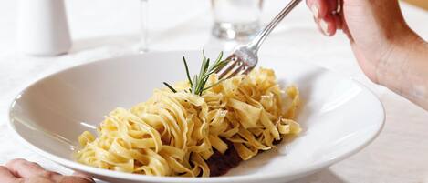 A plate of pasta garnished with rosemary, a fork, and a glass of red wine on a table.