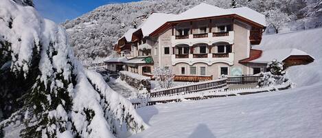 A multi-story hotel with a snow-covered roof and balconies, surrounded by a mountainous landscape.