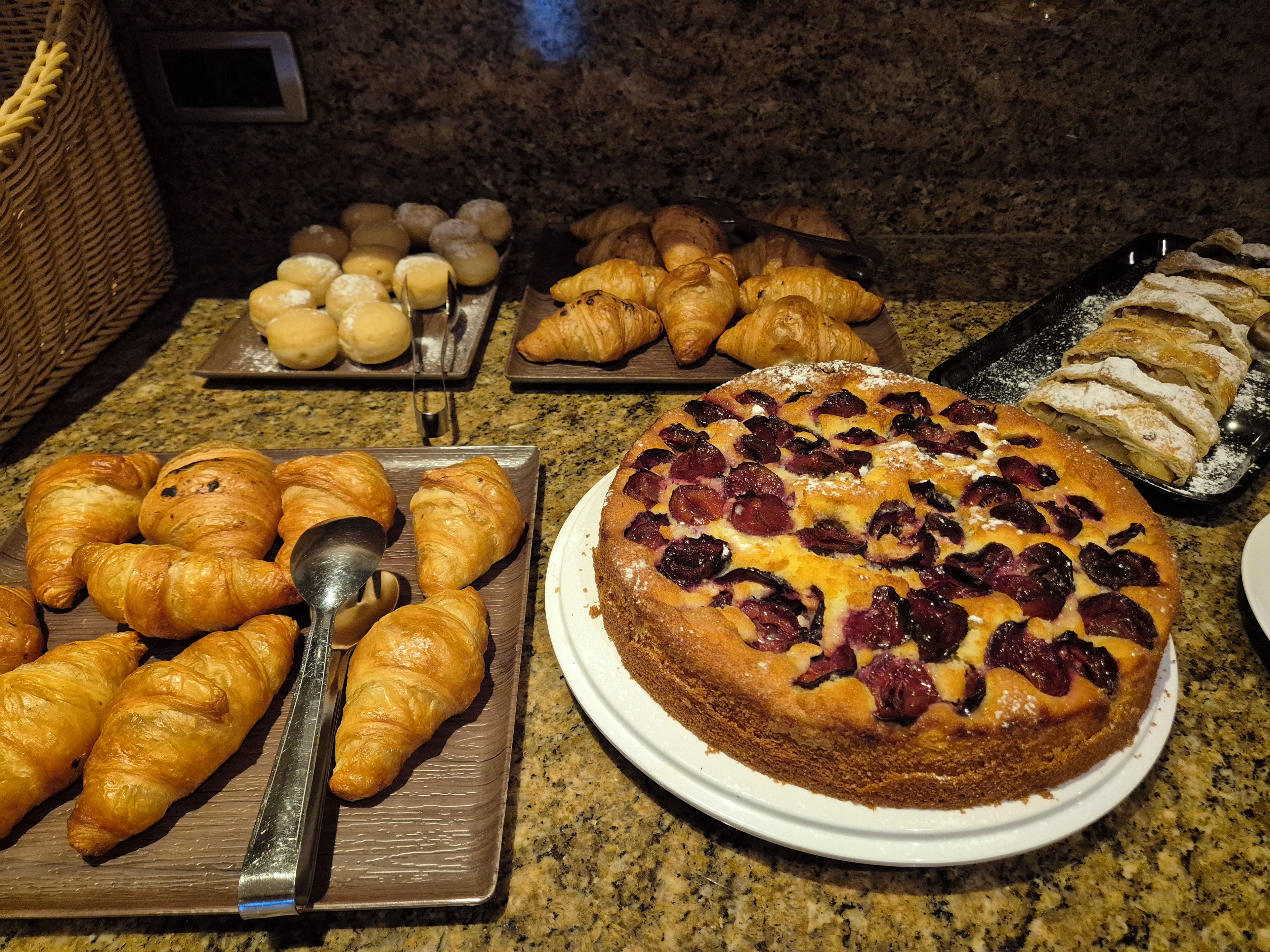 A variety of baked goods including croissants, a pie with fruit, and pastries on a kitchen counter.