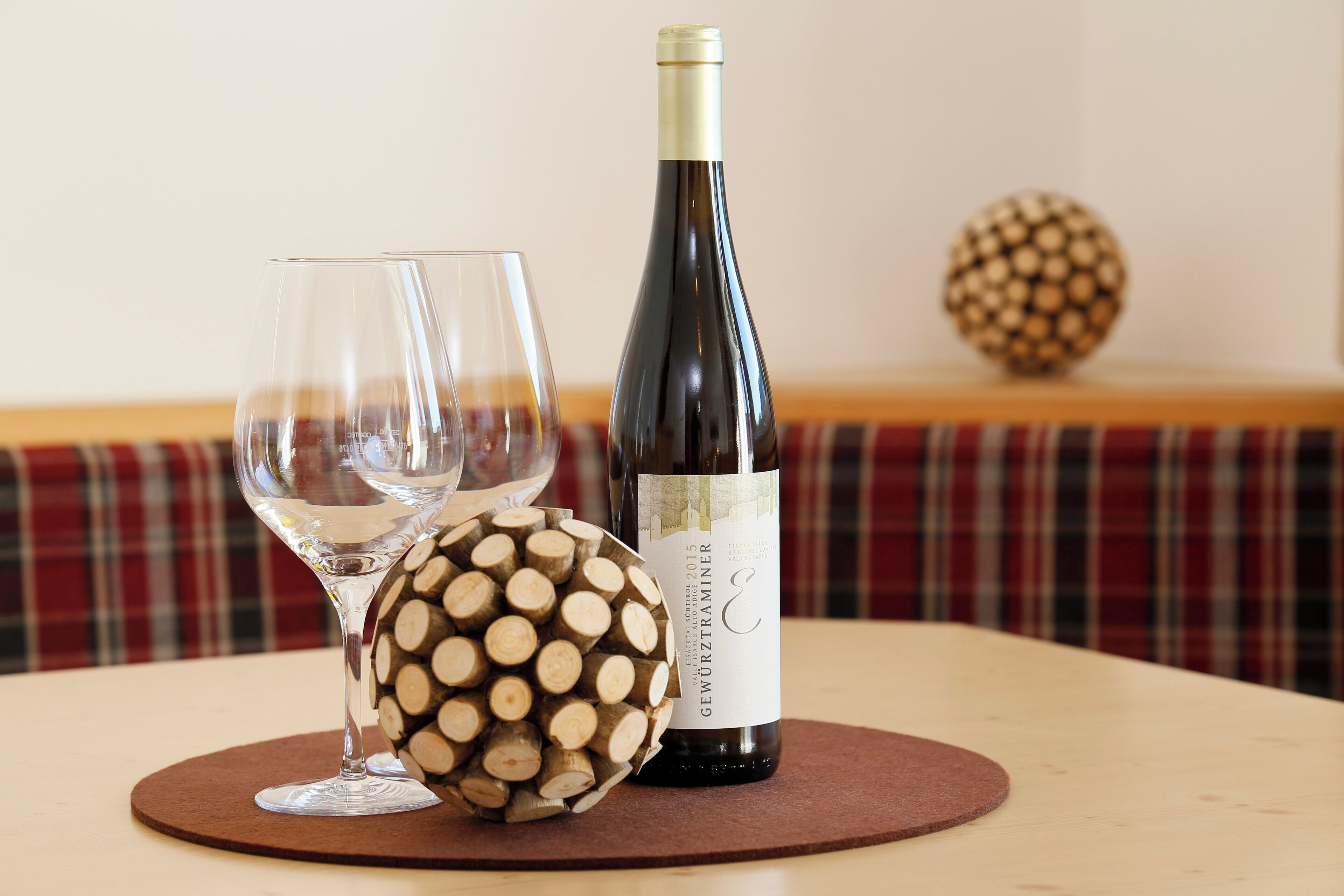A bottle of wine, two glasses, and a decorative wooden sphere on a round table.