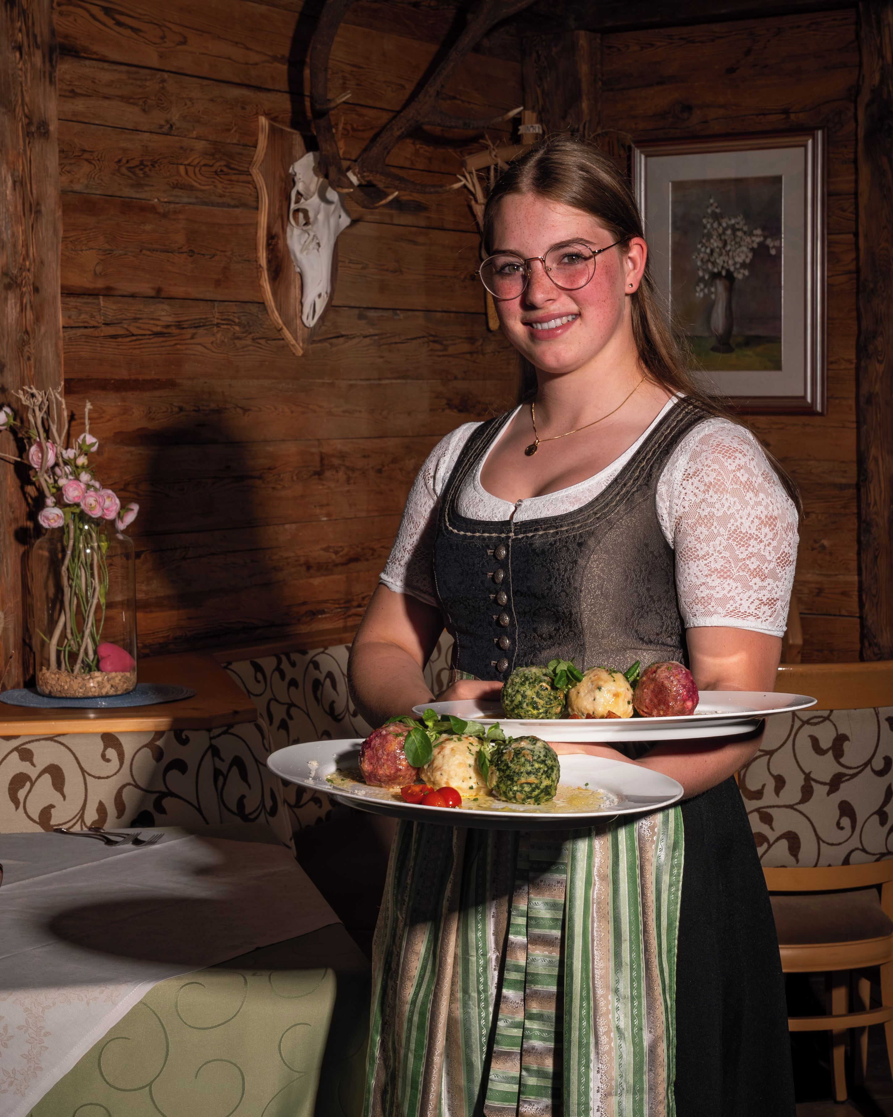 A person holding a plate with food, standing in a room with wooden walls and a deer skull decoration.