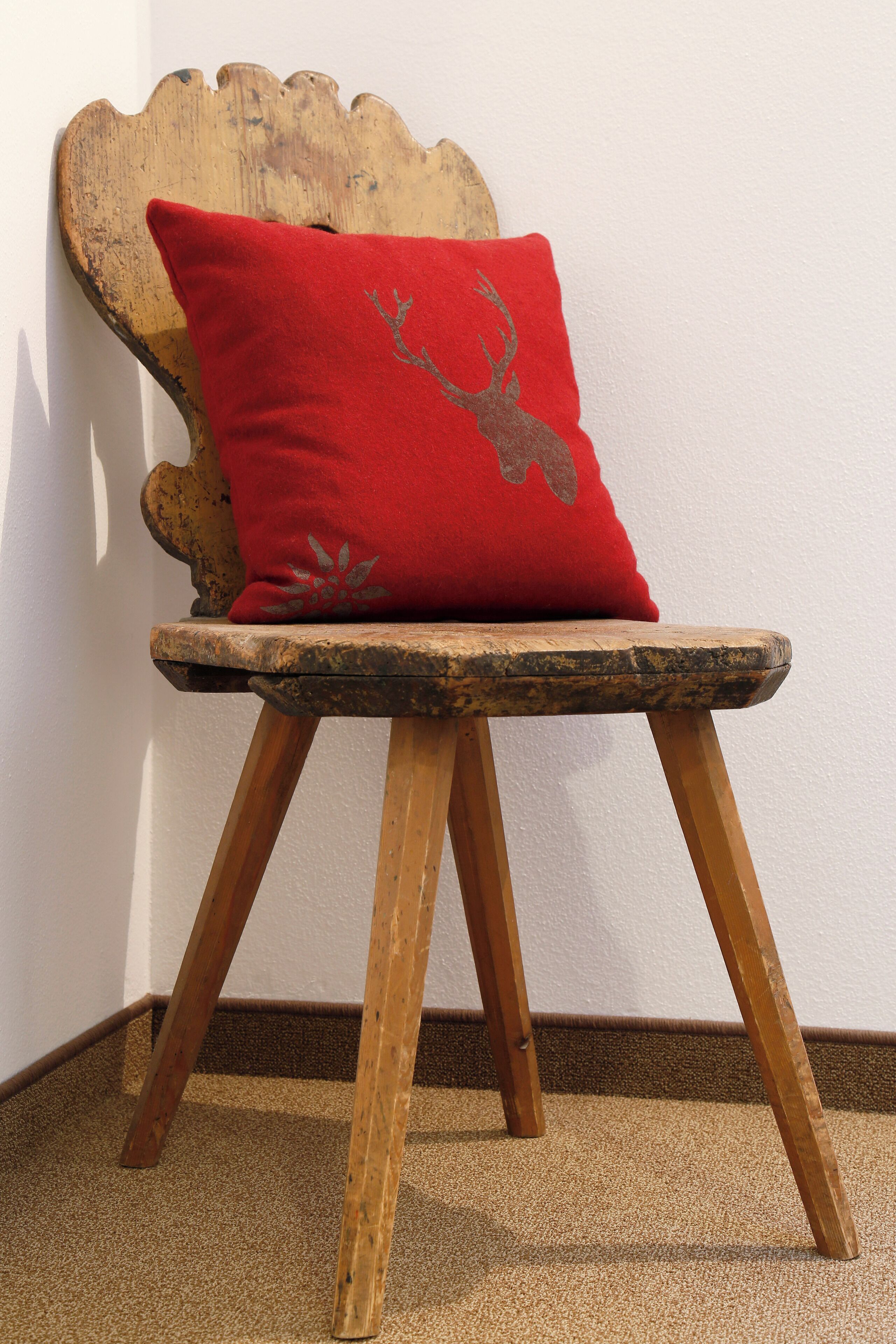 A rustic wooden chair with a red cushion against a white wall.